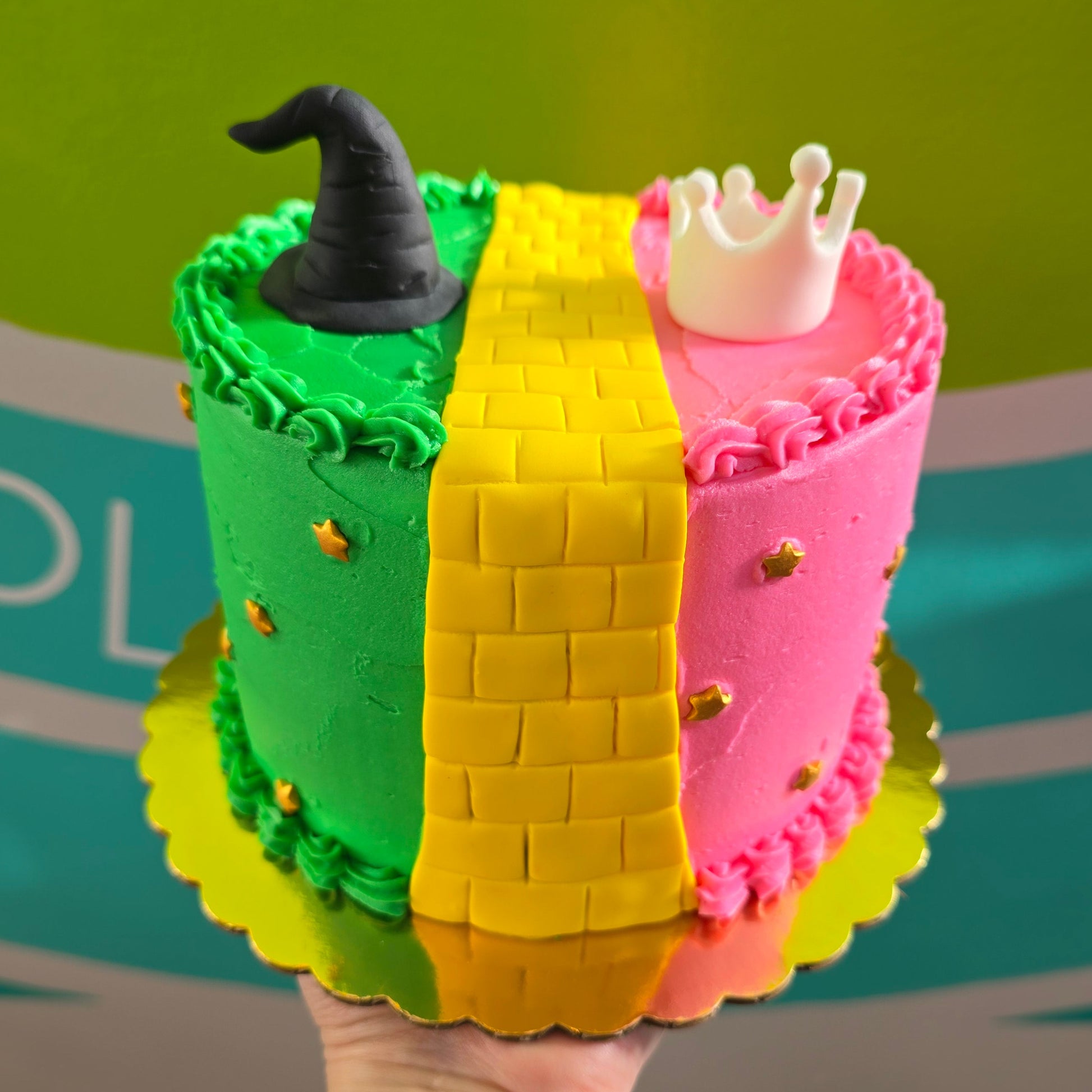 Wicked-themed cake made during cake-decorating class at Cake Hoopla in Tigard near Portland, with pink and green frosting, yellow brick road, and tiara and witches hat.