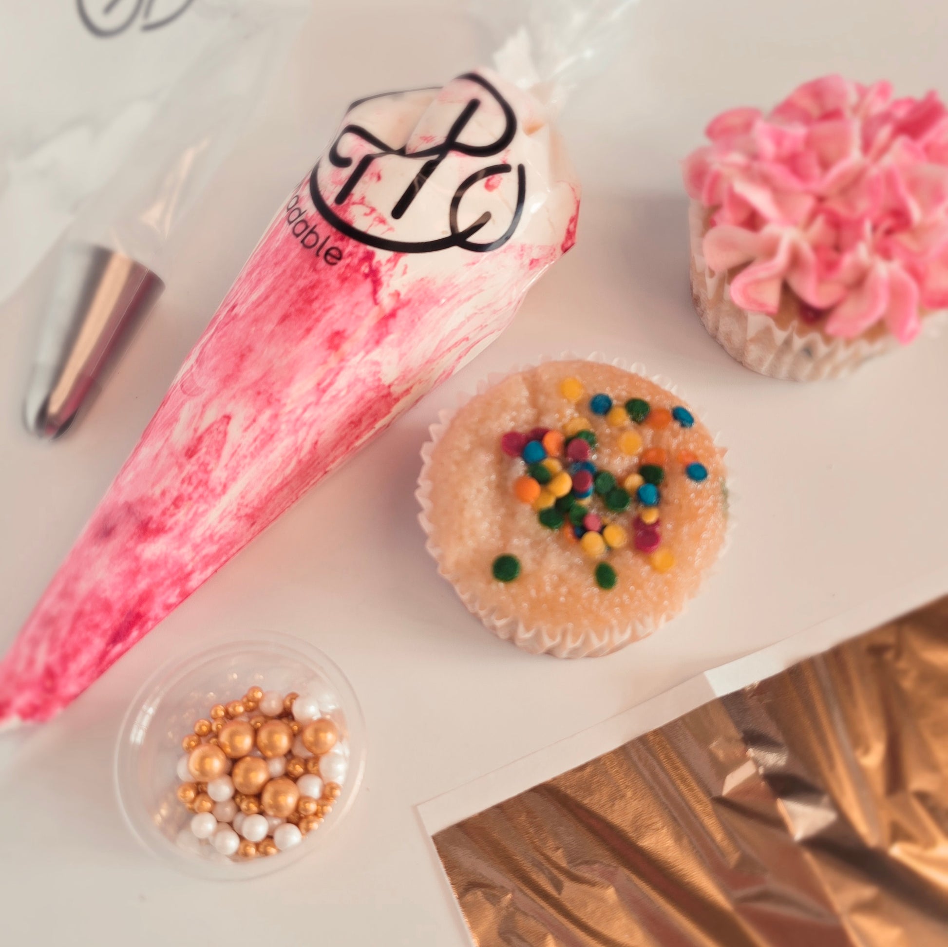 Cupcake with colorful sprinkles next to a piping bag and decorative items on a white surface
