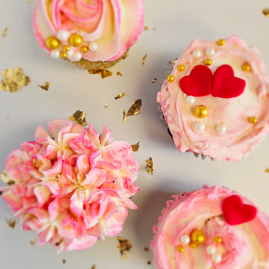 Decorative cupcakes with pink frosting, gold sprinkles, and red heart decorations on a light background.