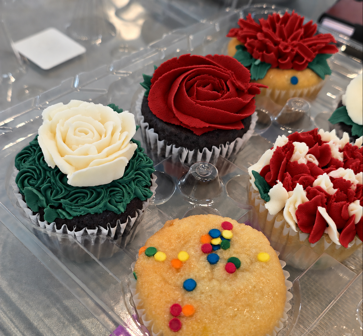 Five Christmas-themed cupcakes with red, green, and white frosting flowers and an unfrosted fetti cupcake in the front.