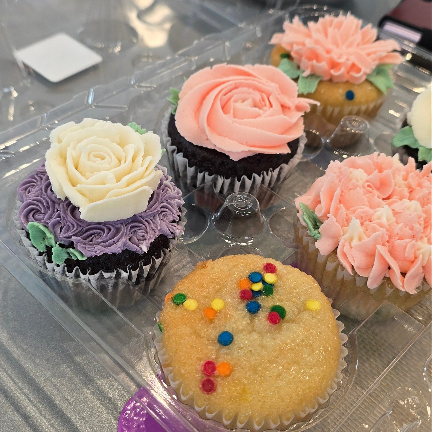 A student's cupcakes, some finished with buttercream flowers, one with no frosting and sprinkles on top.