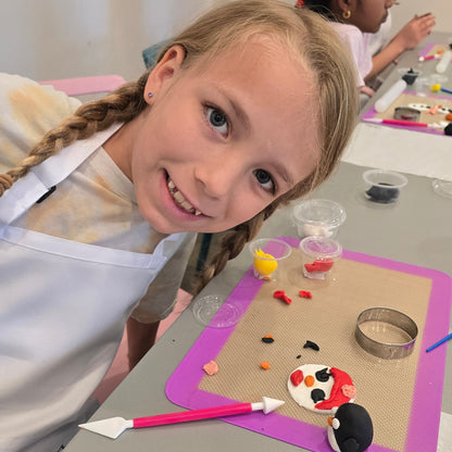 A girl brings her head close to the tabletop with a fondant mat and fondant penguins and snow people she created.