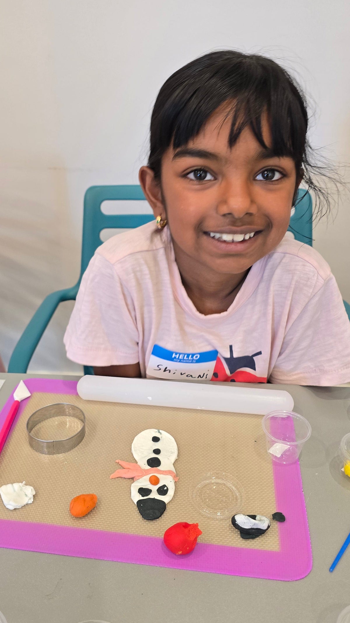 A girl sits in front of her snowman made from white, black, orange, and pink fondant.