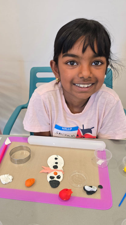 A girl sits in front of her snowman made from white, black, orange, and pink fondant.