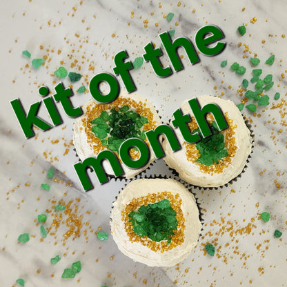 Decorative cupcakes with green and gold sprinkles on a marble surface, featuring text 'kit of the month'.