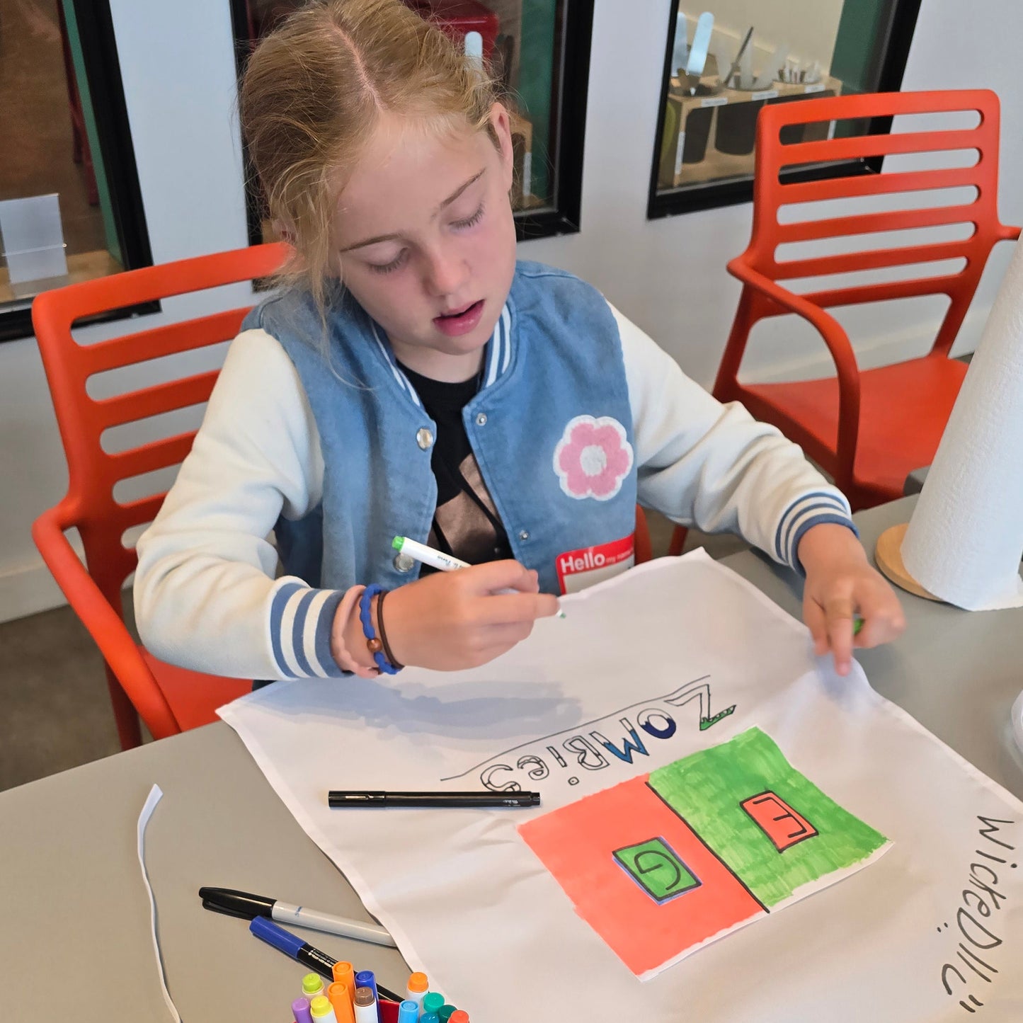 A girl colors a white apron with fabric markers in a zombies theme.