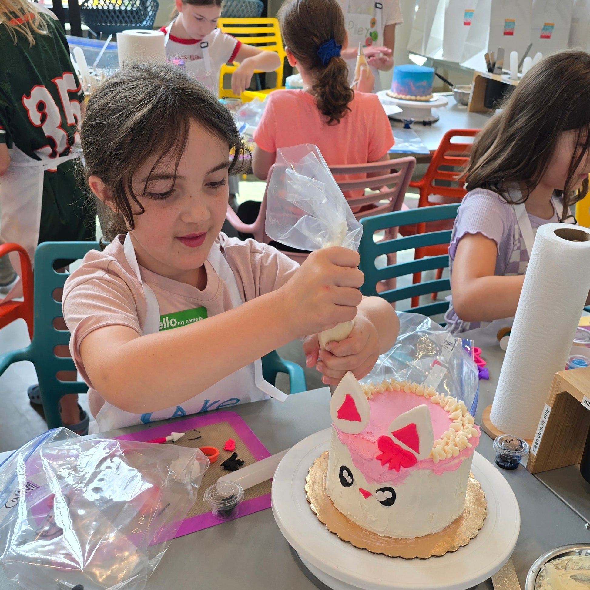 Children decorating cakes in a classroom setting with various decorating tools and ingredients at Cake Hoopla in Tigard, near Portland.