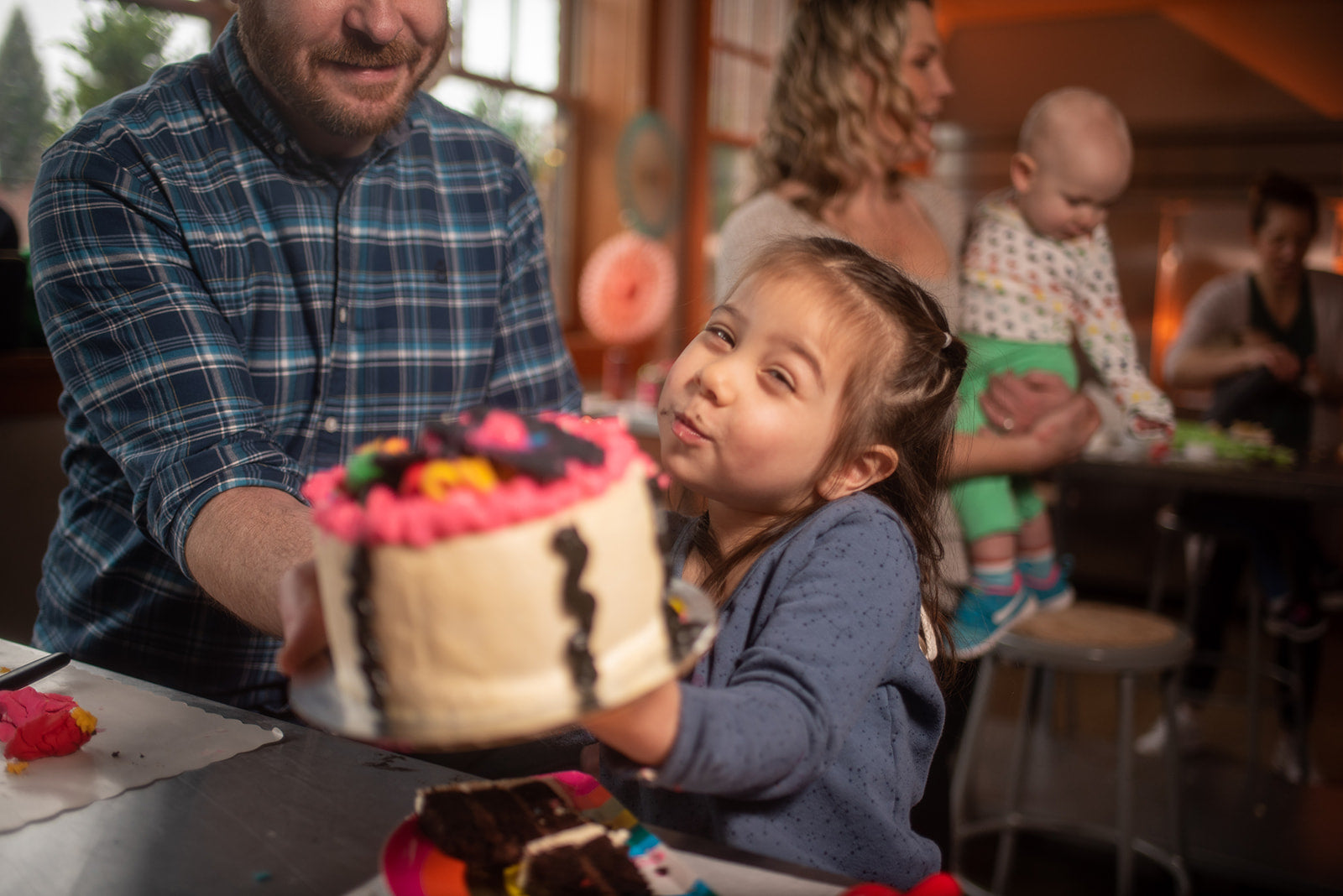 A young child and her dad hold a cake for the camera, showing off their work at a DIY to-go cake-decorating party in the Portland area.