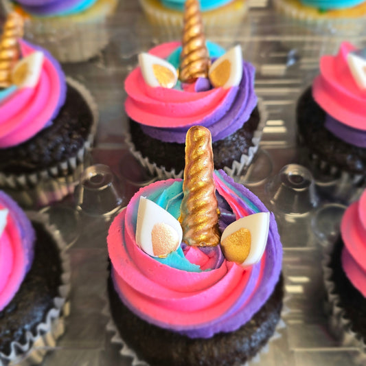 Closeup on chocolate cupcake with pink, purple, and blue swirled frosting, white fondant ears, and gokd accents.