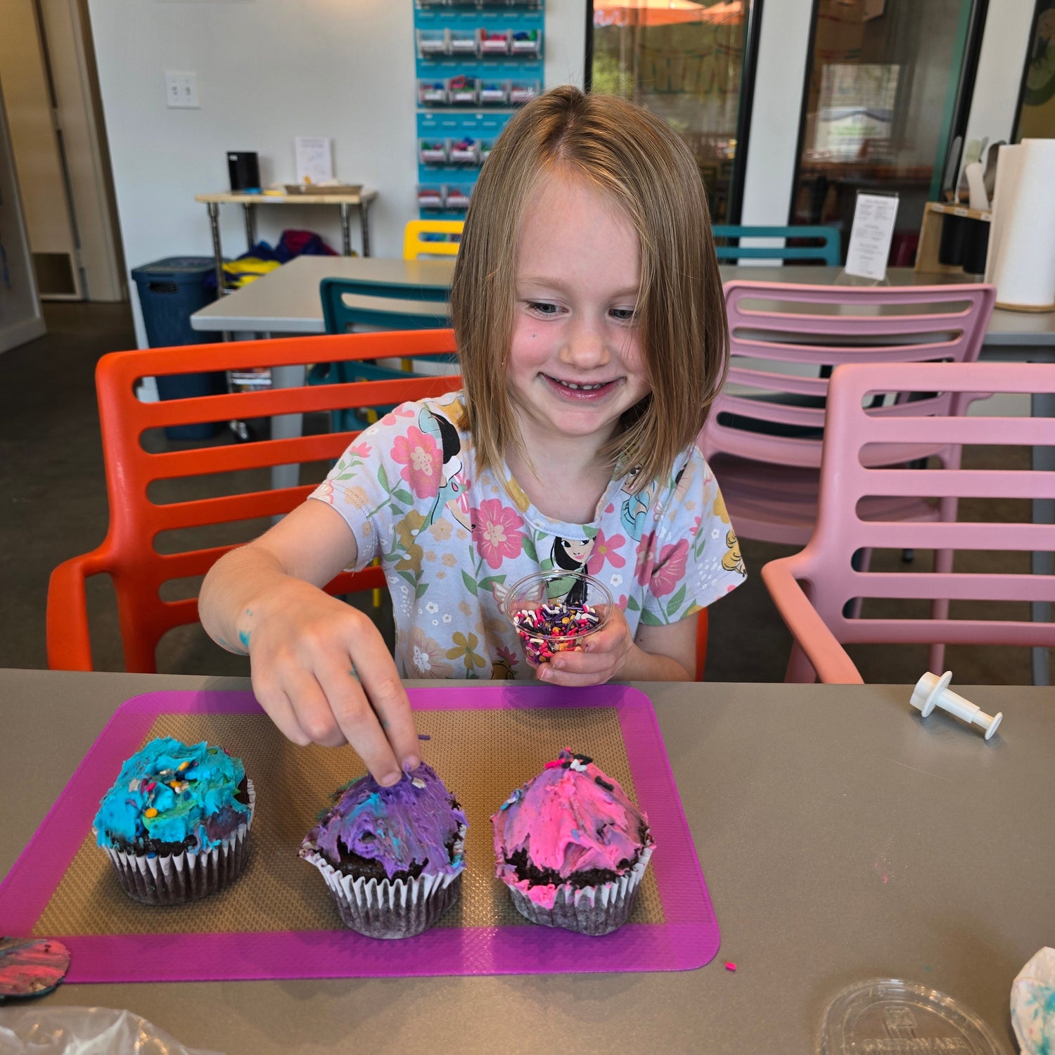 A happy girl decorates colorful cupcakes and add sprinkles at Cake Hoopla's studio in Tigard