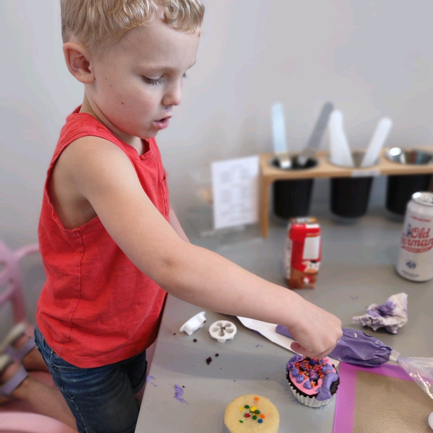A little boy carefuly adds sprinkles to his pink and purple cupcake.