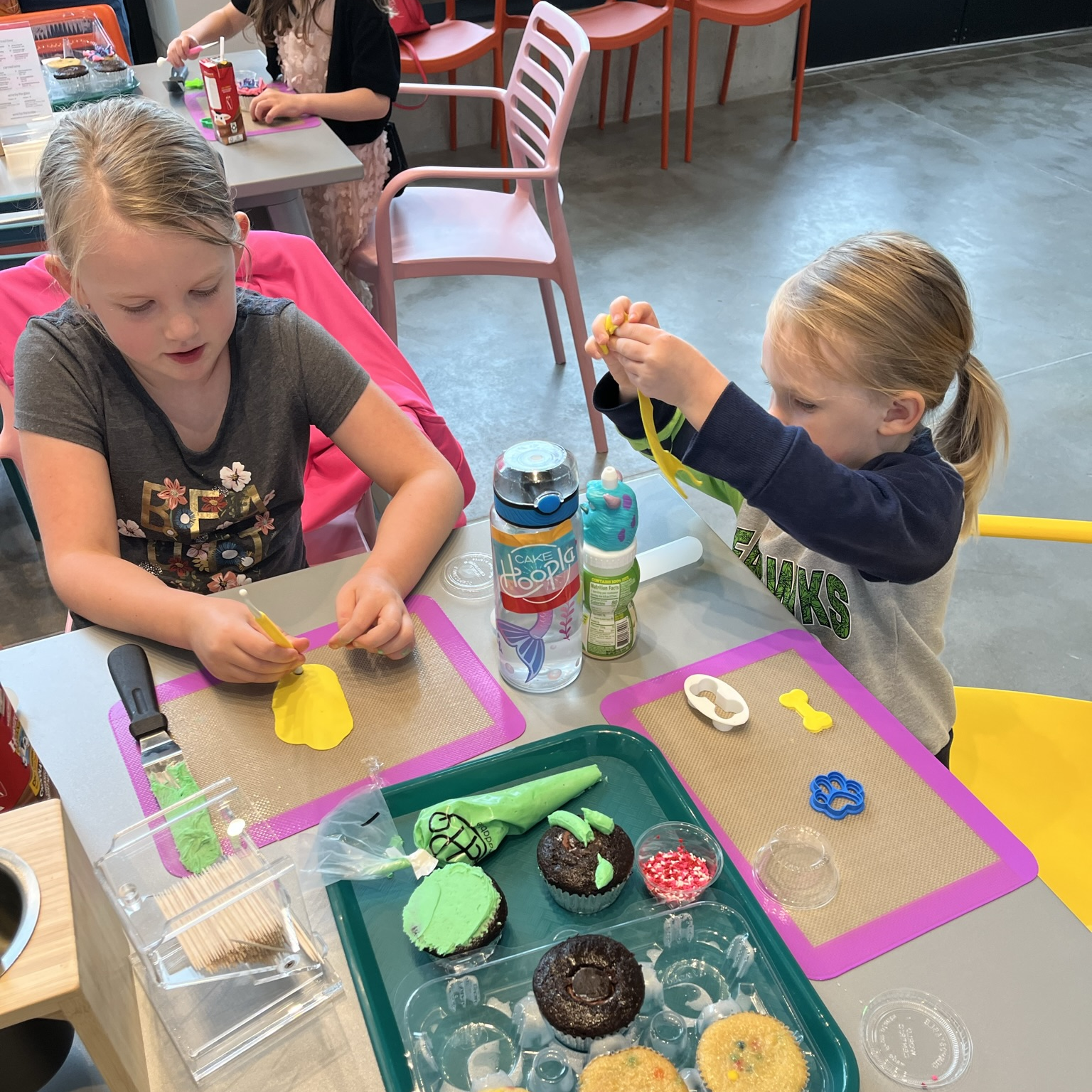 Two little girls decorate cupcakes during open studio time at Cake Hoopla in Tigard, Oregon near Portland.