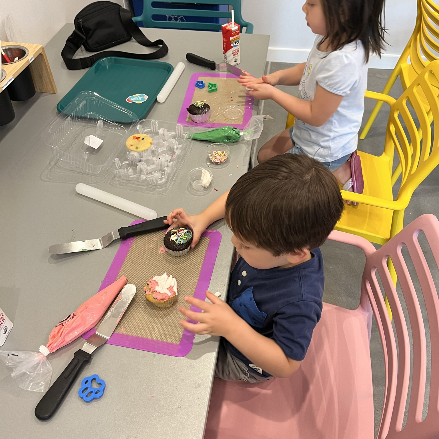 Two young kids concentrate on decorating cupcakes during open studio time at Cake Hoopla in Tigard, Oregon and in the Portland area.