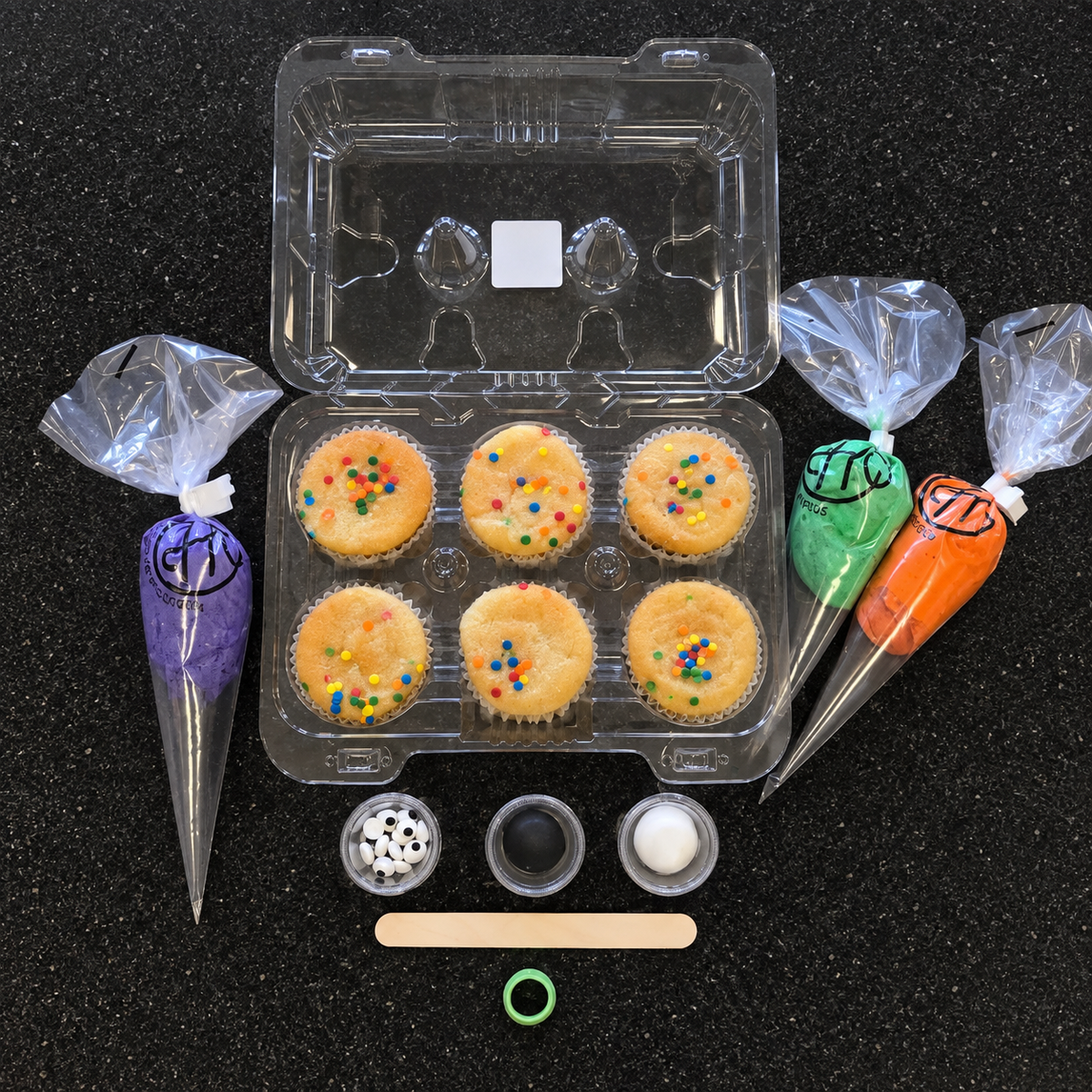 The contents of the Monster Creepcakes cupcake kit, including cupcakes, purple, green, and orange frosting, fondant, candy eyes and decorating tools.