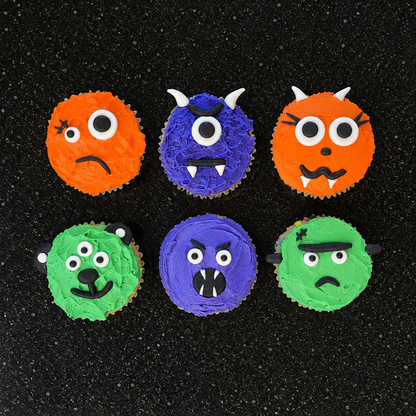 Orange, purple, and green monsters with different scary facial features, like scars, three yes, horns, and fangs, decorated in a Halloween motif on a black stone background.