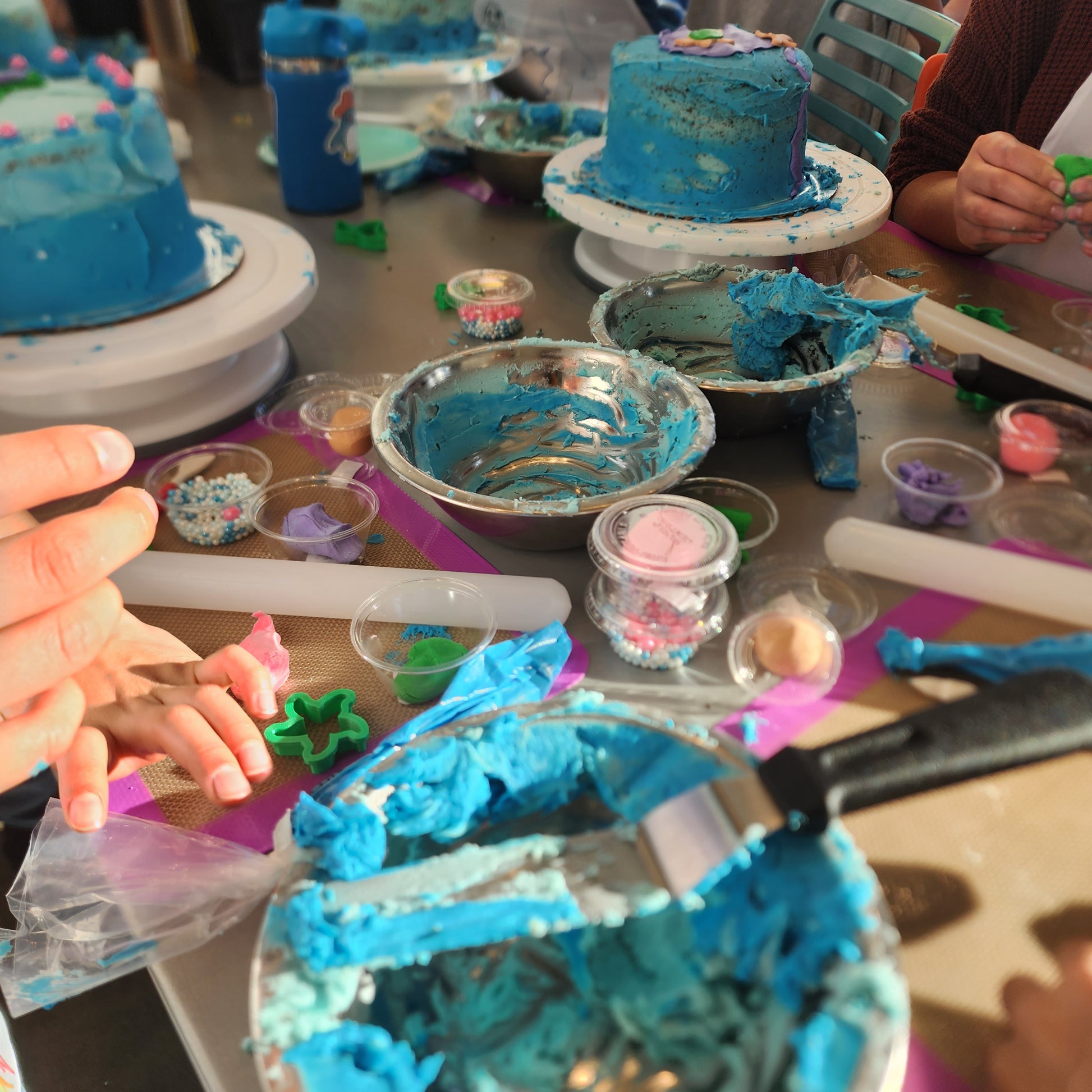 A table full of cake-decorating supplies, including ocean-blue frosting, a variety of fondants, and cakes beautifully frosted in shades of blue for an under-the-sea-themed cake-decorating party at Cake Hoopla in Tigard, near Portland.