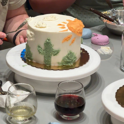 A close up on a dessert-themed palette knife cake with cacti and an orange sun with glasses or red and white wine in the foreground.