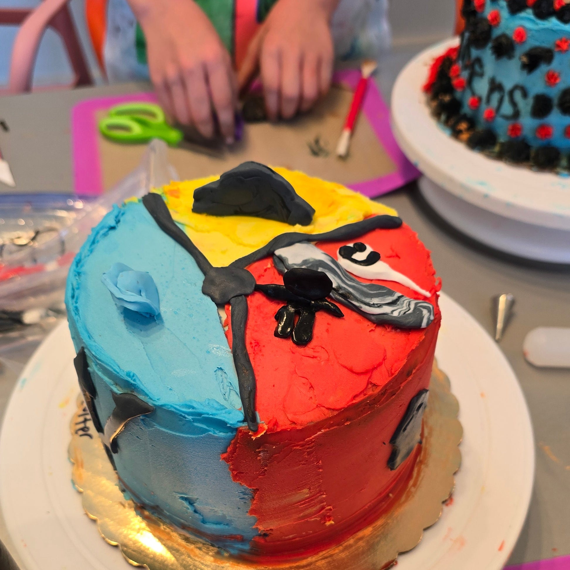Colorful cake with a character design on a table with various items during Cake Hoopla summer cake camp.