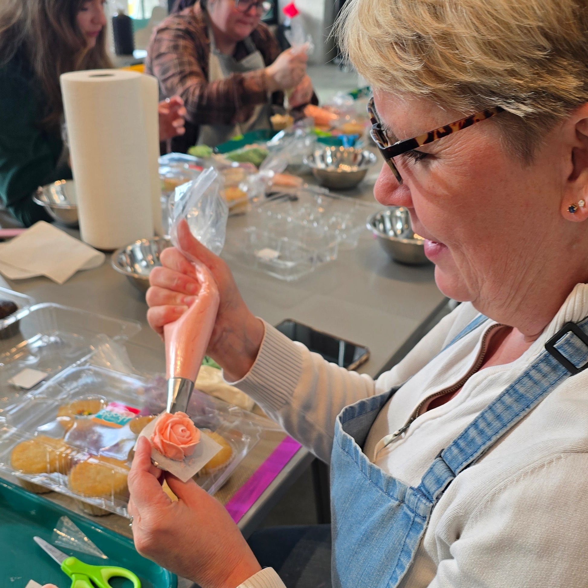 Woman pipes rose with pink buttercream on frosting nail at Cake Hoopla in Tigard, near Portland.