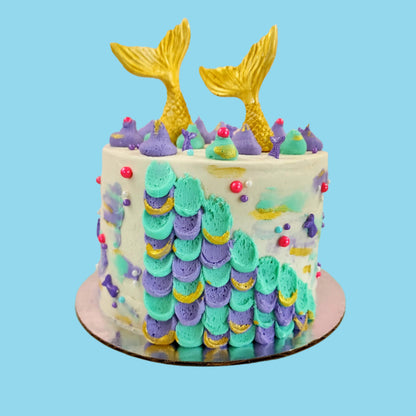 Mermaid cake with teal and purple frosting, gold mermaid tails, and pink and purple sprinkles; a DIY cake kit available to decorate during open studio time at Cake Hoopla in Tigard, Oregon, in the Portland area.