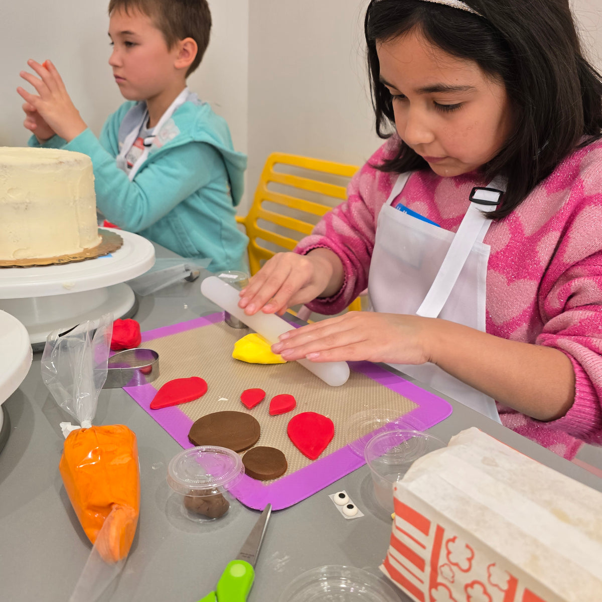 A girl rolls out pieces of her fondant turkey to go on top of her white cake.