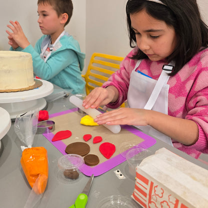 A girl rolls out pieces of her fondant turkey to go on top of her white cake.