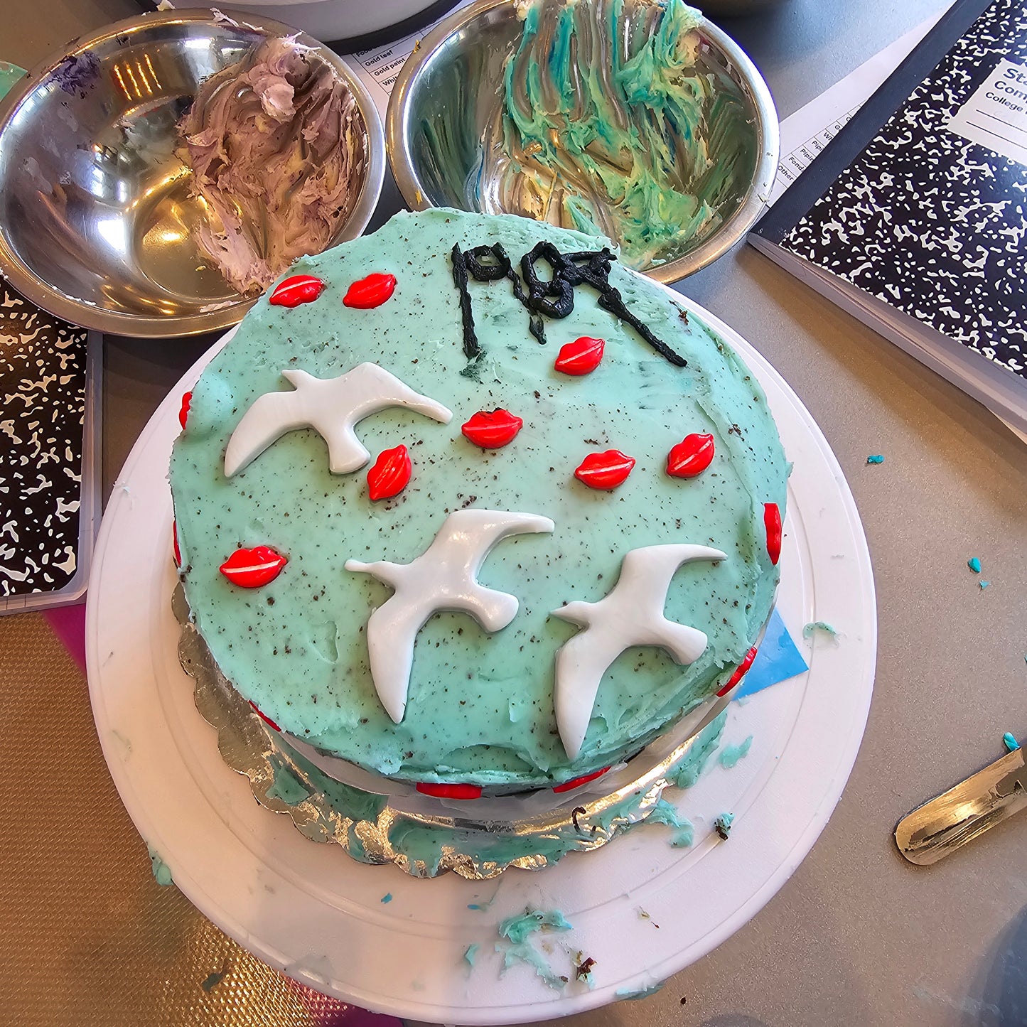 1989 Taylor Swift themed cake with teal frosting, white birds, and red lips by a camper at Cake Hoopla summer cake camp.