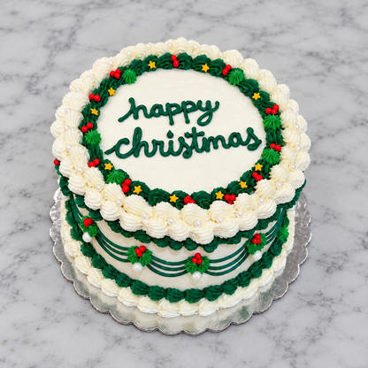 White cake with white and light and dark green frosting borders, red and gold star sprinkles, and "happy christmas" written in dark green frosting on top of the cake.
