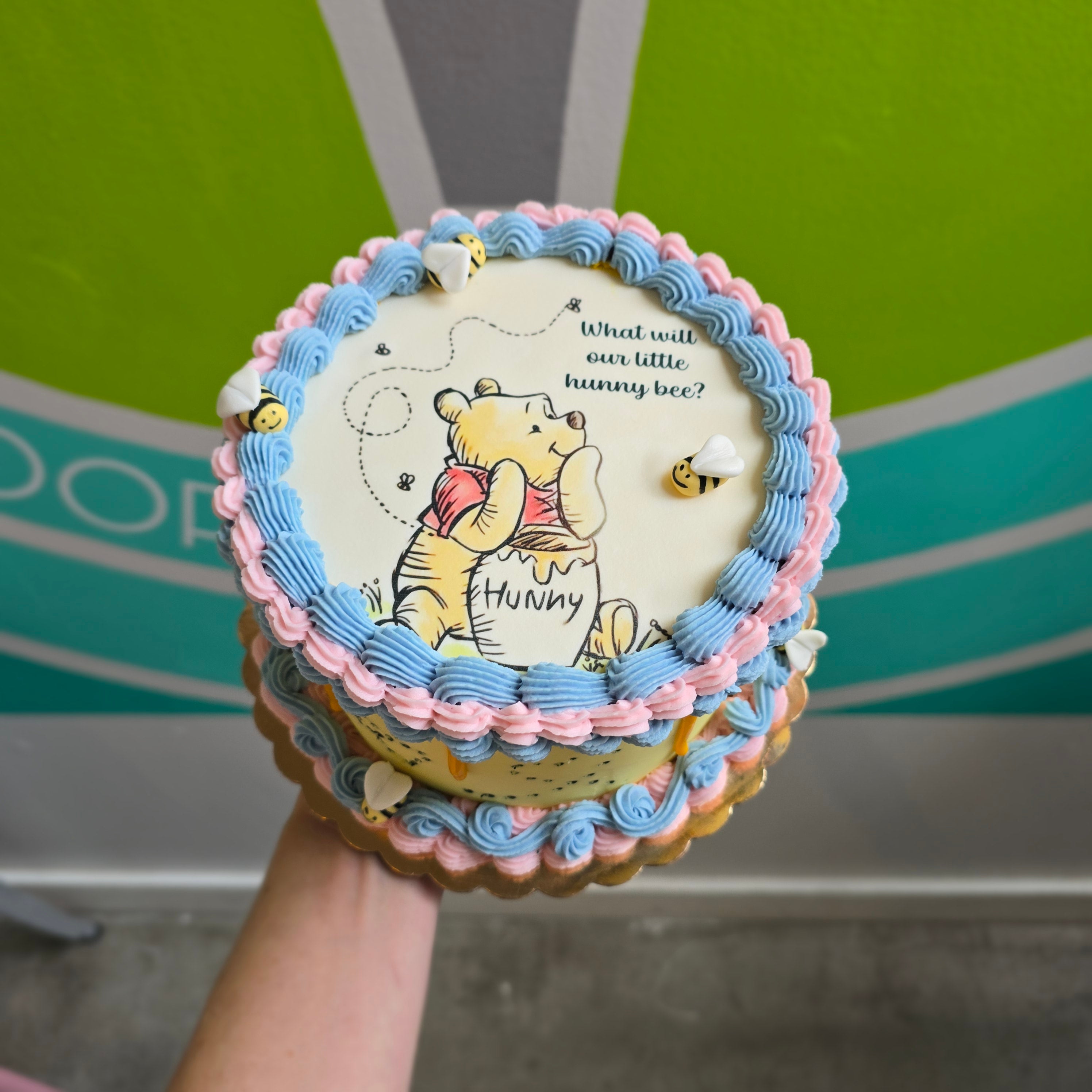 Winnie the Pooh baby shower cake with "What will our little hunny bee" design and edible fondant bees.