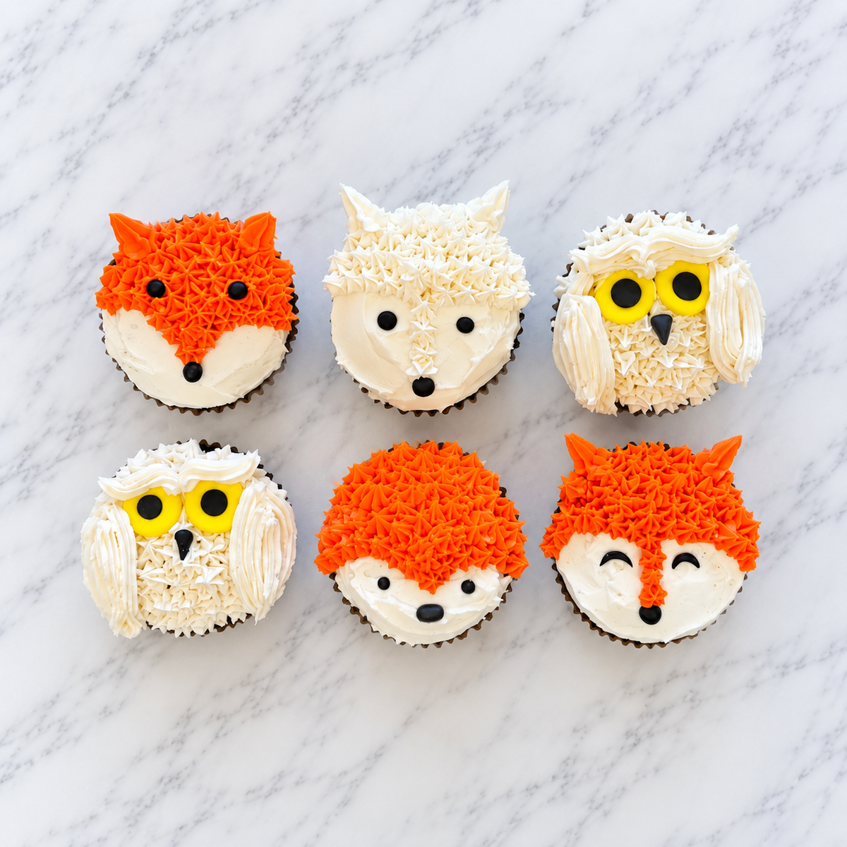 6 cupcakes, with 2 orange and white foxes, 1 white fox, 1 white own, and 1 orange and white hedgehog, all with frosting starsa nd fondatn faces.