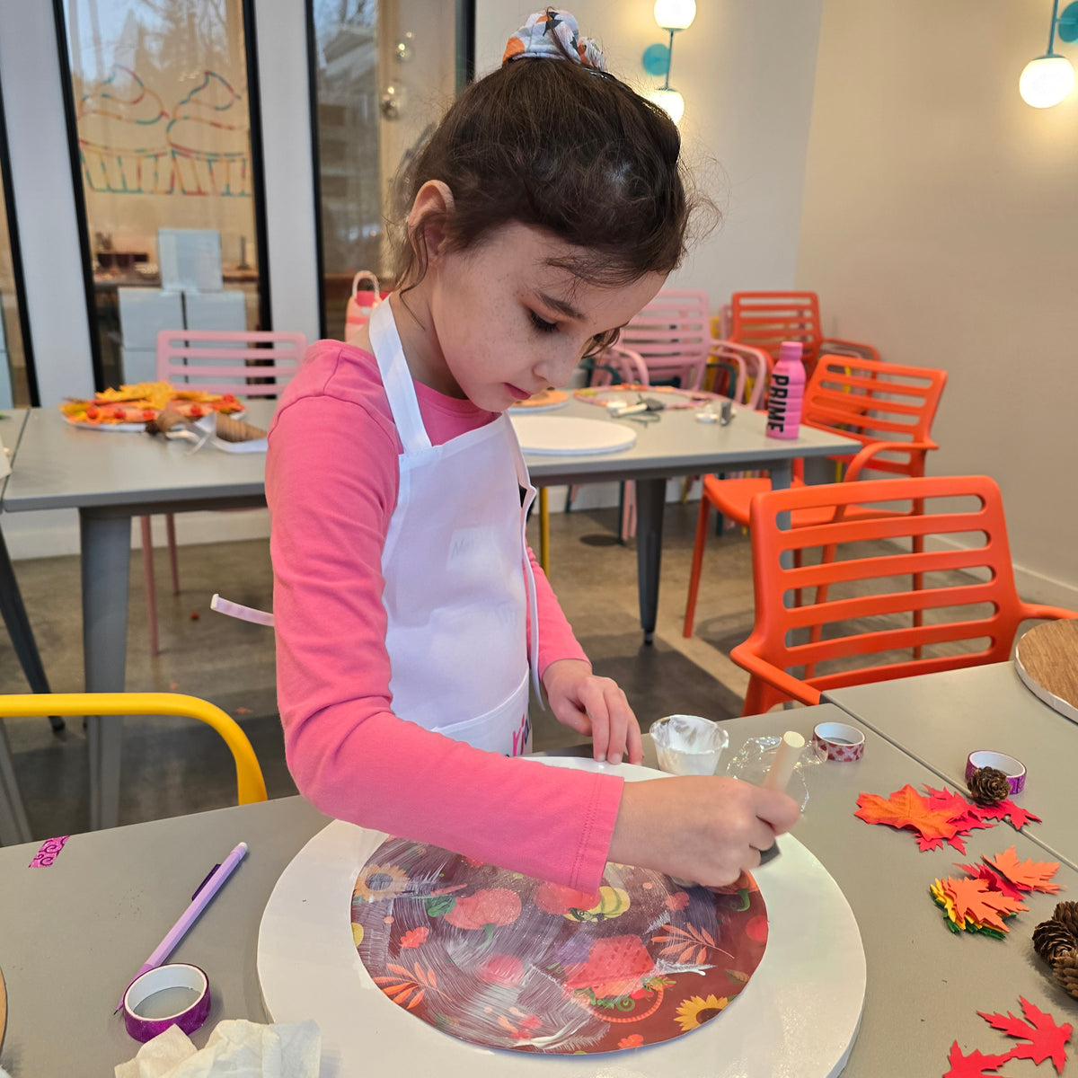 A girl works on her harvest craft project using glue, paper in a fall motif, and colorful autumn leaves.