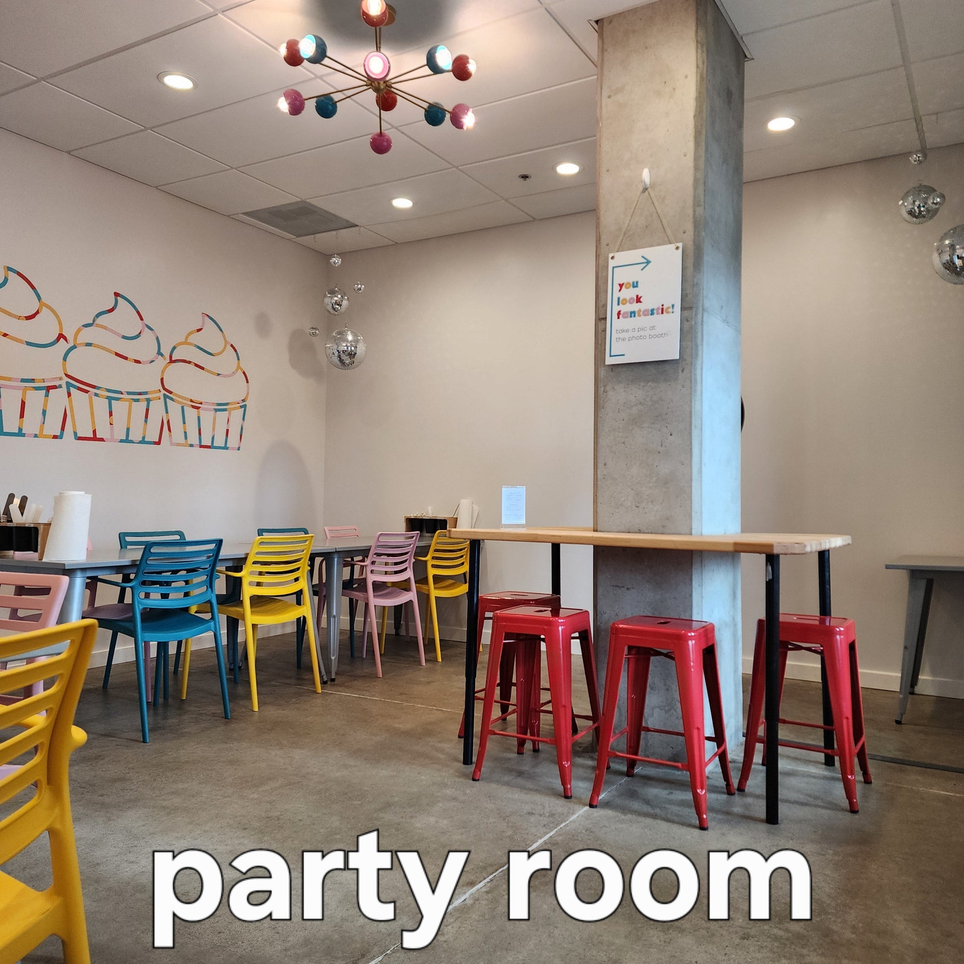 Cake Hoopla's party room, with several tables and bright-colored chairs, chandelier, disco balls and decorations, available to rent for DIY cake/cupcake-decorating parties and events in Tigard, near Portland.