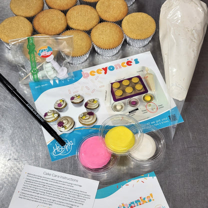 The components of the "beeyonce's" DIY cupcake-decorating kit, including 12 cupcakes, pink, yellow, and white fondant, a black edible marker, white frosting, fondant cutters, and white frosting.