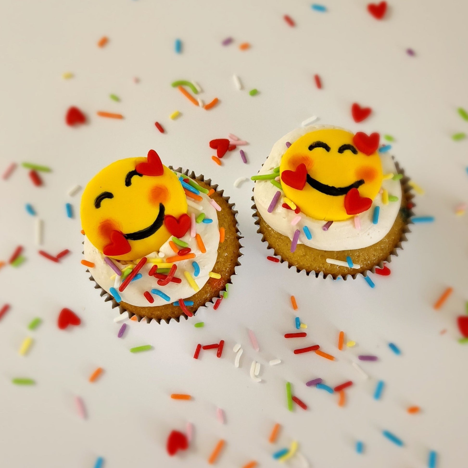 Two finished cupcakes from the Happy Hearts Emoji DIY cupcake-decorating kit available for open studio time, as a to-go kit, or as pre-decorated cupcakes from the Cake Hoopla in Tigard, Oregon near Portland