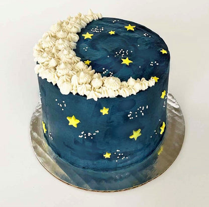 A moon-themed dark blue cake with a white crescent moon piped on the top with yellow fondant stars and white sprinkle galaxies dotting the cake; a pre-decorated cake shipped to the continental US.