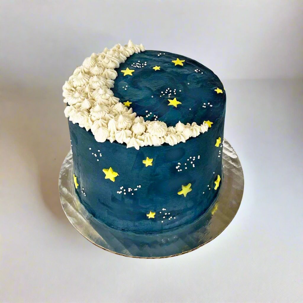 To The Moon cake decorated like a night sky with a white crescent moon, yellow stars, and sprinkle galaxies, available as a DIY cake-decorating kit during open studio time or to-go or as a pre-decorated kit from Cake Hoopla in Tigard, Oregon near Portland