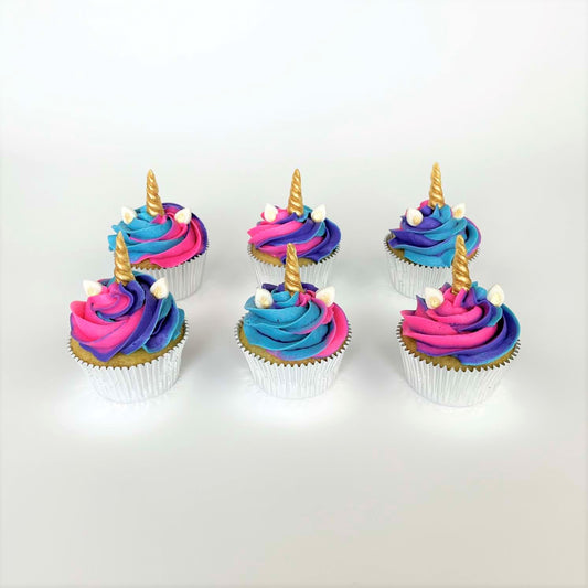 Several finished unicorn-themed cupcakes from the Myth Makers cupcake kit. They have swirls of bold pink, purple and blue frosting topped with gold-painted white chocolate unicorn hors and white fondant ears painted gold in the center. These cupcakes are whimsical and on theme with many children’s birthday party themes.