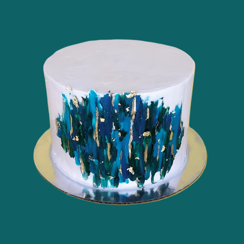 A white cake with teal, dark blue, and dark green streaks of frosting, like a giclee painting, and gold accents; a pre-decorated cake shipped to the continental US.