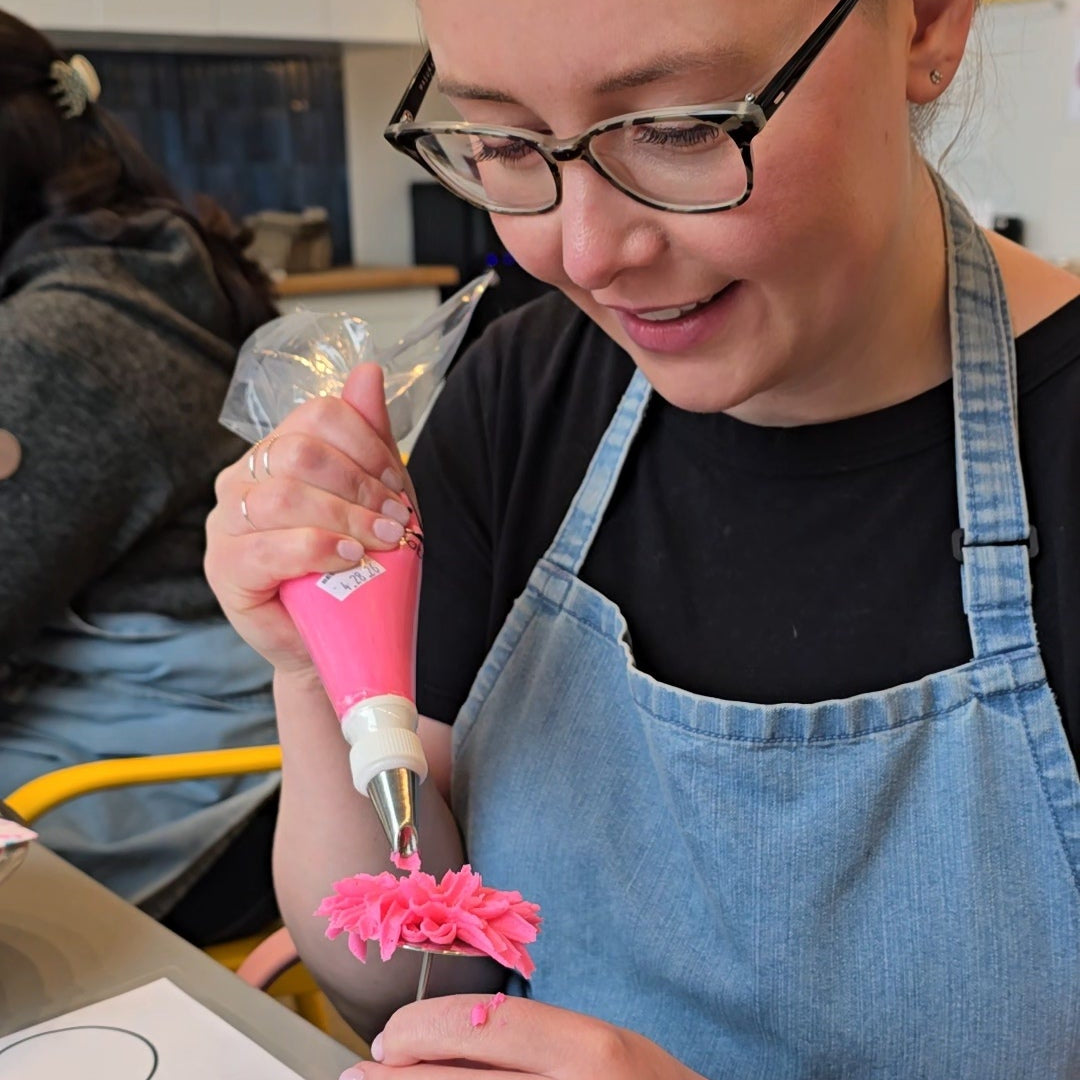 Woman pipes mum flower with pink buttercream on frosting nail at Cake Hoopla in Tigard, near Portland.