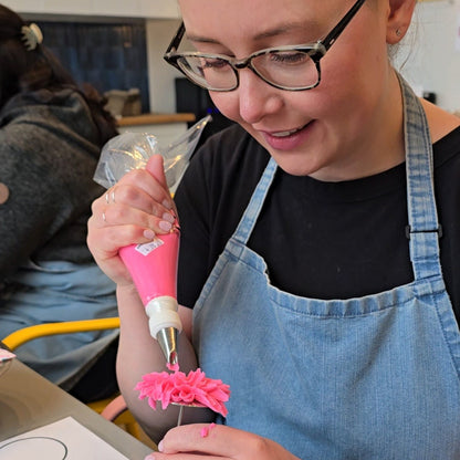 Woman pipes mum flower with pink buttercream on frosting nail at Cake Hoopla in Tigard, near Portland.