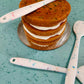 Several silicone spatulas lay on top of and around an unfrosted three-layer Fetti cake. These spatulas would be handy for frosting the cake. 