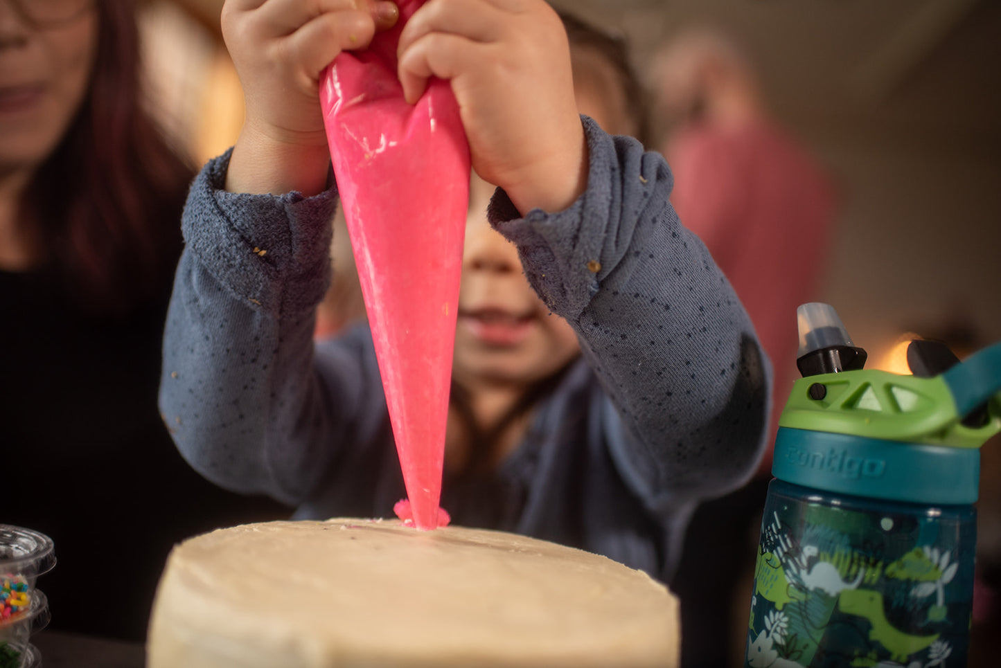 A little girl is at a custom DIY cake decorating party in the Portland area. She is squeezing pink frosting out of a piping bag and onto a cake. 