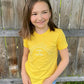 An eight-year-old girl wears the “sunshine & sprinkles” t-shirt. The color is vibrant and pops against her skin. The design in the center of the t-shirt spans horizontally almost all the way across her chest. 