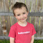 A five-year-old boy with a sly smile wears the babycakes and hoopla t-shirt.
