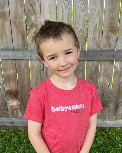 A five-year-old boy with a sly smile wears the babycakes and hoopla t-shirt.