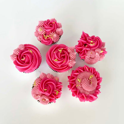 Finished cupcakes from the DIY La Fleur cupcake kit are frosted with bright pink and light pink rosettes, pointy stars, and little swirls. Small amounts of gold leaf highlight each cupcake. The cupcakes are bright and vibrant, and each has a different design, showing that you can get creative with the final look. These are elegant, yet fun DIY cupcakes.