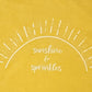 A closeup of the screen printing on the “sunshine & sprinkles t-shirt. “Sunshine & sprinkles” is written in a whimsical, almost cursive font across the center. The words are framed by an abstract half sun with rays of sprinkley sunshine shooting out. 