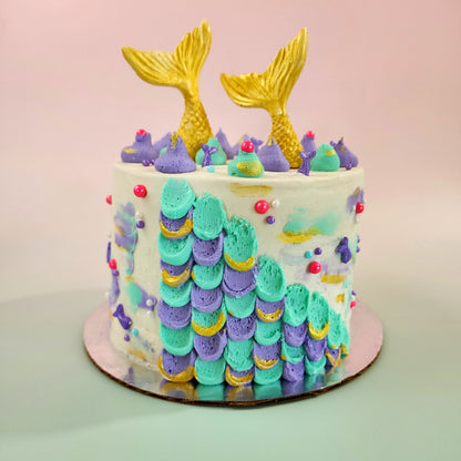 Mermaid cake with teal and purple frosting, gold mermaid tails, and pink and purple sprinkles; a pre-decorated cake available for pick up at Cake Hoopla in Tigard, Oregon, in the Portland area.