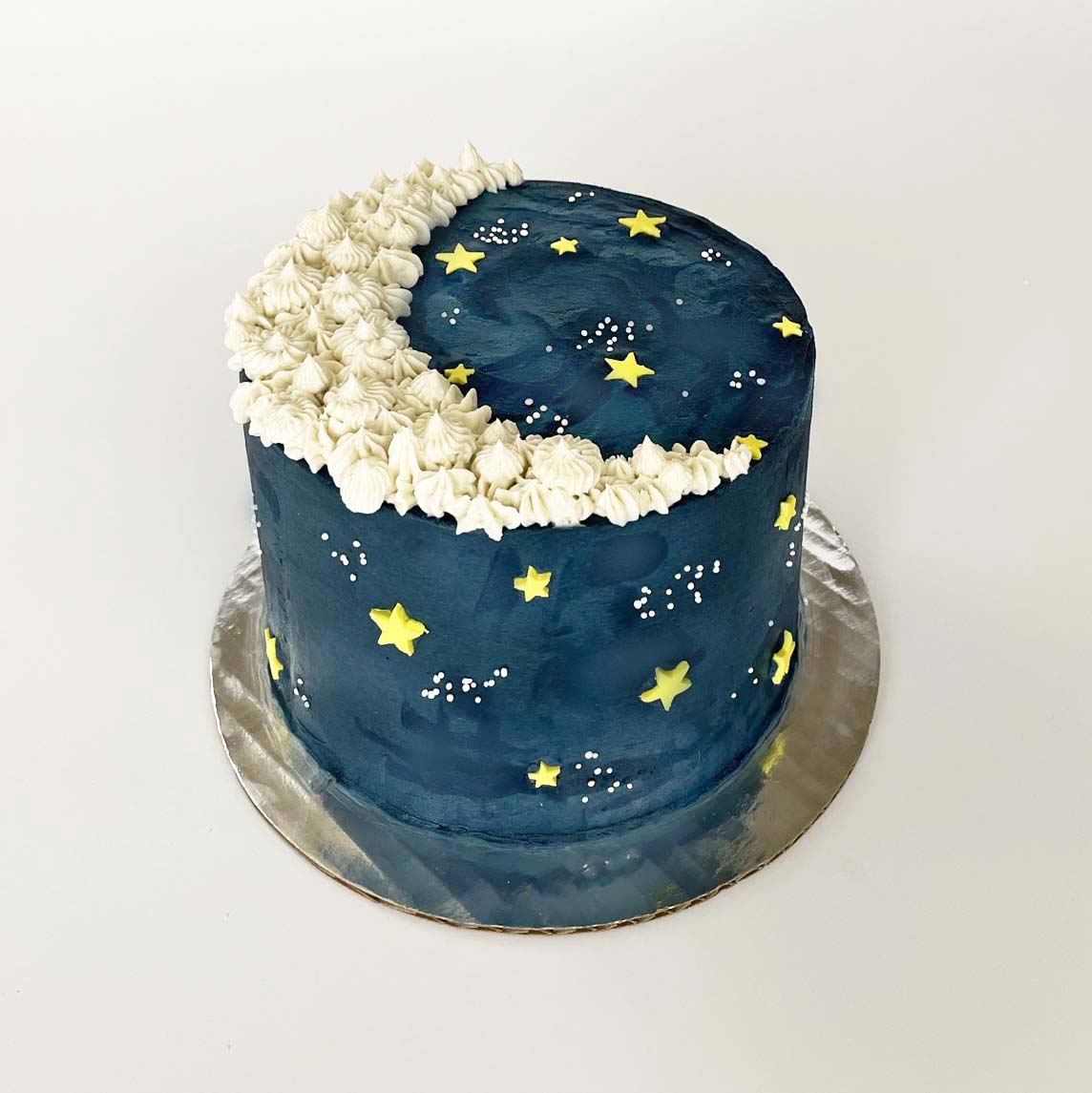  This DIY cake is a whimsical version of the night sky. The cake is coated in dark blue frosting and a crescent moon piped in white frosting across the top. Yellow fondant stars and little constellation of tiny white ball-shaped sprinkles are pressed over the front and sides.